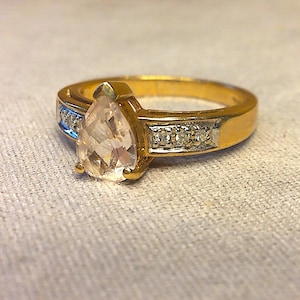 以下が含まれることがあります： 梨型の透明な石と小さな透明な石のバンドが付いた金の指輪