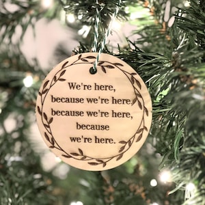 May include: A round wooden bauble with a brown, engraved design of leaves and the text "We're here, because we're here, because we're here, because we're here."