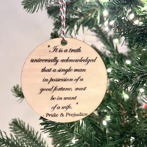 May include: A round wooden bauble with a white string hanging from the top. The bauble has a quote from Pride and Prejudice engraved on it: "It is a truth universally acknowledged that a single man in possession of a good fortune, must be in want of a wife." - Pride & Prejudice
