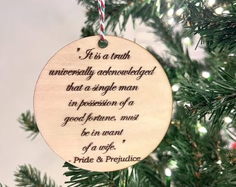 May include: A round wooden ornament with a white string hanging from the top. The ornament has a quote from Pride and Prejudice engraved on it: "It is a truth universally acknowledged that a single man in possession of a good fortune, must be in want of a wife." - Pride & Prejudice