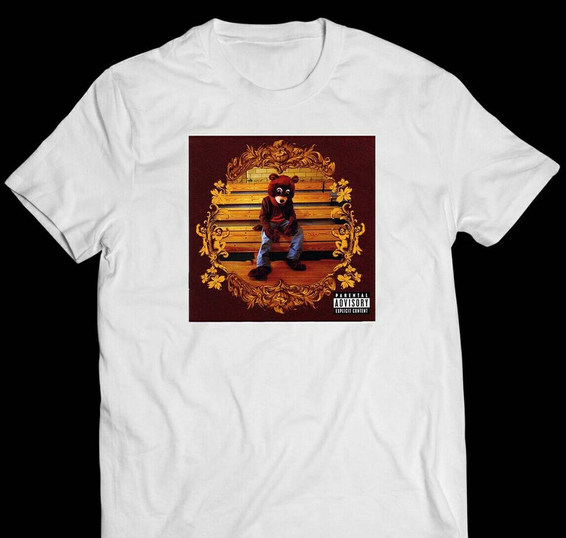 May include: White t-shirt with a graphic print of a bear wearing a mask and sitting on a bench. The graphic is surrounded by a gold frame and has a Parental Advisory label.