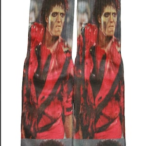 May include: A pair of black and gray socks with a colorful image of a person wearing a red jacket. The image is repeated on both socks.