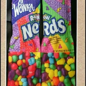 May include: A pair of colorful socks with a Nerds candy design. The socks feature the Wonka logo and the words "Rainbow Nerds".
