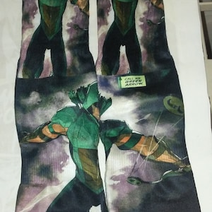 May include: A pair of black and green socks with a graphic print of Green Arrow, a comic book superhero. The socks have the text "Call me Green Arrow." printed on them.