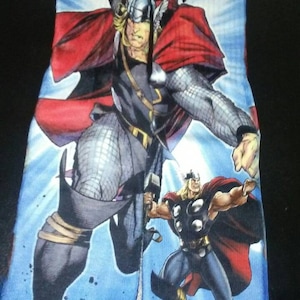 May include: A pair of socks featuring a comic book illustration of Thor, the Marvel Comics superhero. The design includes multiple images of Thor in action, with a blue background and red accents. The word "Thor" is visible in red.