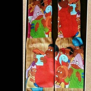 May include: A pair of colourful socks with a cartoon design featuring a group of people. The socks are brown with a wood grain pattern and feature a variety of characters with different skin tones and hairstyles. The characters are wearing various outfits, including hats, shirts, and trousers. The socks are a fun and unique way to add a touch of personality to any outfit.