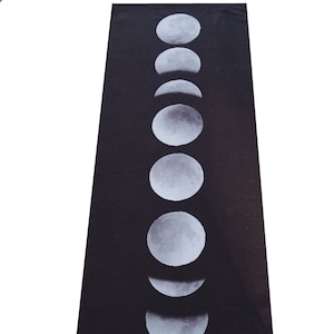 May include: Black yoga mat with a white moon phases design. The mat has the text "yoga zeal" printed on the bottom.