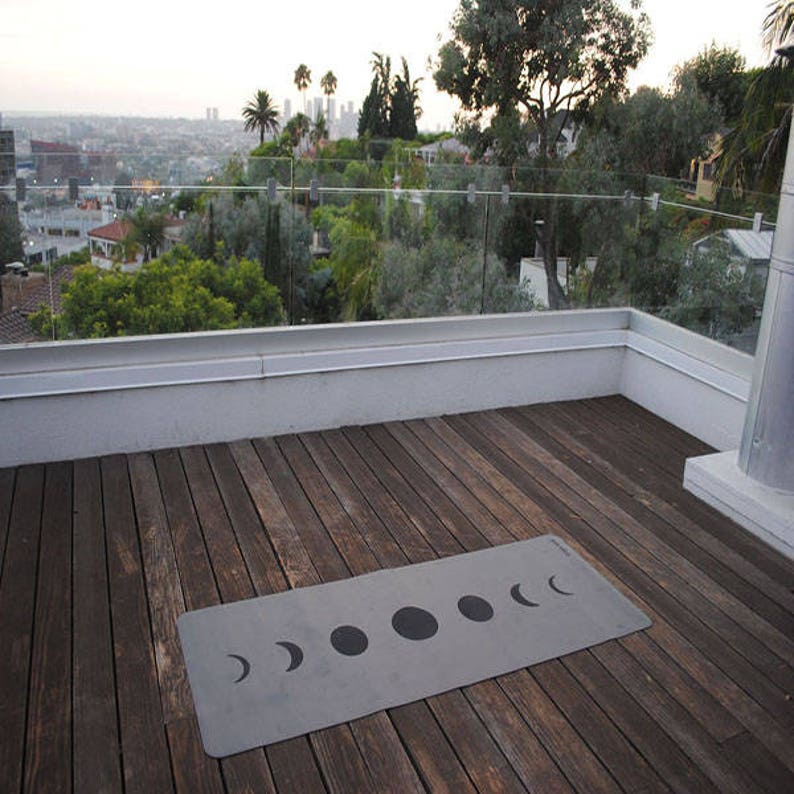 May include: A grey yoga mat with a black moon phase design on a wooden deck overlooking a city skyline.