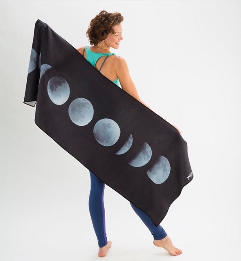 May include: A black yoga mat with a moon phase design. The mat has a white "yoga" logo in the bottom right corner.