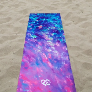 May include: A yoga mat with a colorful abstract design featuring shades of blue, pink, and purple. The mat has a white logo in the center.