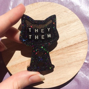 Pin con pronombre "Ellos/Ellas" de gato negro con purpurina: broche de resina Enby hecho a mano, cara seria