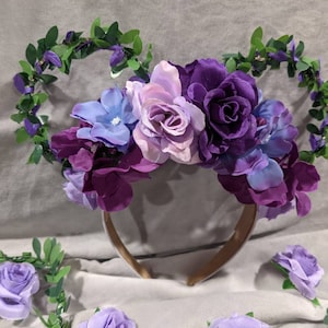 May include: Purple, pink, and blue flower headband with green leaves. The headband is made of a brown fabric and has a floral design.