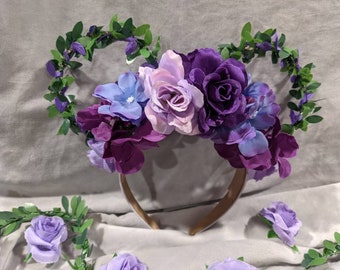 May include: Purple, pink and blue flower headband with green leaves. The headband is made of a brown fabric and has a floral design.