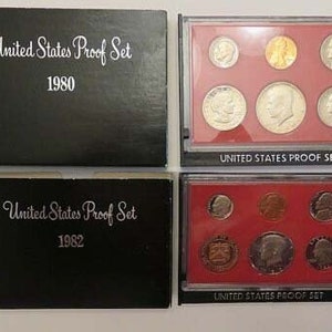 May include: Two black boxes with the text "United States Proof Set" and the years 1980 and 1982. Each box contains a set of silver coins.