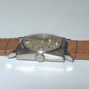May include: A silver wristwatch with a square face and a brown leather band.