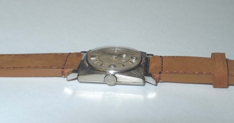 May include: A silver wristwatch with a square face and a brown leather band.