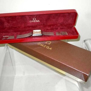 May include: A red and brown watch box with the Omega logo on the lid. The watch is inside the box and has a silver band.