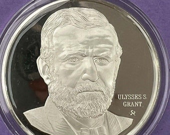 May include: A silver coin with a portrait of Ulysses S. Grant, the 18th President of the United States. The coin has the inscription "ULYSSES S. GRANT" and a copyright symbol.