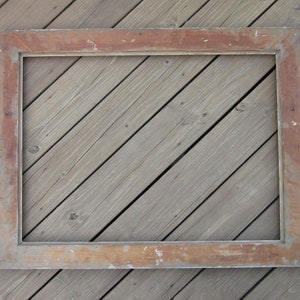 May include: A large, rectangular, wooden picture frame with a white painted finish. The frame has a slightly distressed look, with some of the wood showing through the paint. The frame is lying flat on a wooden surface.