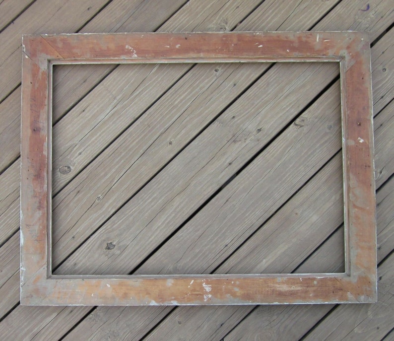 May include: A large, rectangular, wooden picture frame with a white painted finish. The frame has a slightly distressed look, with some of the wood showing through the paint. The frame is lying flat on a wooden surface.