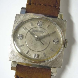 May include: A silver square-shaped wristwatch with a brown leather band. The watch face has a silver background with black Roman numeral hour markers and a silver second hand. There are three small diamonds on the watch face.