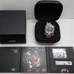 Puede incluir: Un reloj Oris plateado con una esfera negra y una ventana de fecha. El reloj est&aacute; en una caja negra con un estuche de reloj negro. El reloj viene con un manual de producto y un folleto de servicio internacional.