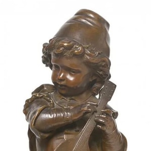May include: A bronze sculpture of a young person wearing a cap and playing a guitar. The sculpture is detailed and realistic, with a focus on the person's facial expression and the instrument.