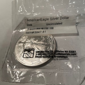 K&ouml;nnte beinhalten: Eine silberne American Eagle Dollar-M&uuml;nze in einem Plastikbeutel. Die M&uuml;nze ist mit 2009 datiert und ungezirkelt. Der Beutel tr&auml;gt ein Etikett mit der Aufschrift "Littleton Coin Co., Littleton NH 03561, 1-800-645-3122, LittletonCoin.com, Priced according to condition".