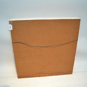 May include: The reverse side of a framed picture, featuring a brown wooden panel with a hanging wire. A small white tag with the number "333" is attached to the upper left corner. The artwork is set against a white backdrop.