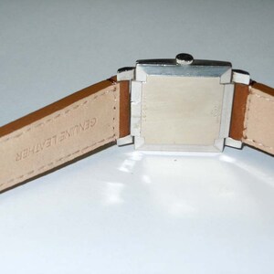 May include: A silver square watch with a brown leather band. The band is labeled "Genuine Leather".