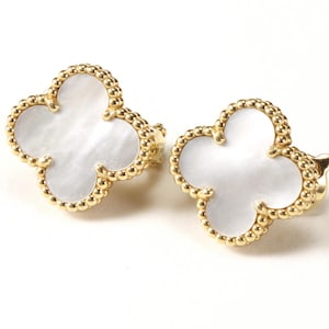May include: A pair of gold stud earrings, each featuring a four-leaf clover shape with a white mother-of-pearl inlay. The edges of the clover are defined by a beaded gold border, creating a textured, metallic frame around the smooth, iridescent white center.
