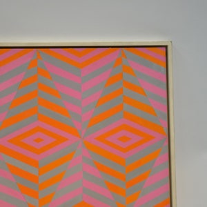 May include: Abstract geometric artwork with a repeating diamond and chevron pattern. The design incorporates grey, orange, and pink hues, producing a striking visual impact. The artwork is presented within a white wooden frame.