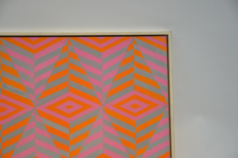 May include: Abstract geometric artwork with a repeating diamond and chevron pattern. The design incorporates grey, orange, and pink hues, producing a striking visual impact. The artwork is presented within a white wooden frame.