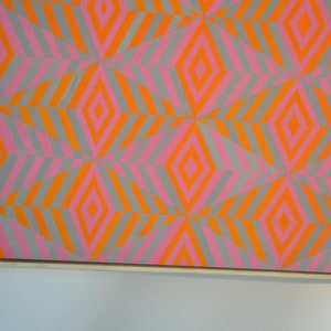 May include: Abstract artwork with a repeating geometric pattern of diamonds and diagonal stripes. The design uses orange, pink, and grey. The artwork is framed. The colour scheme creates a vibrant visual effect.