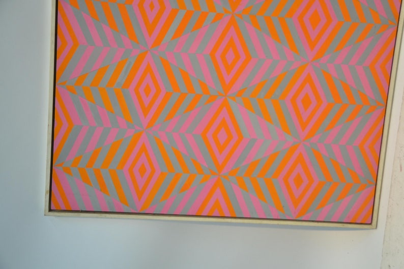 May include: Abstract artwork with a repeating geometric pattern of diamonds and diagonal stripes. The design uses orange, pink, and grey. The artwork is framed. The colour scheme creates a vibrant visual effect.