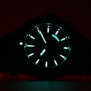 Puede incluir: Un reloj de pulsera negro con una esfera verde luminosa y agujas plateadas. La esfera del reloj tiene una ventana de fecha y un segundero. El reloj est&aacute; iluminado en la oscuridad.