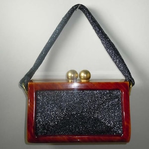 May include: A black beaded evening bag with a brown tortoise shell frame and gold-toned clasps. The bag has a black beaded shoulder strap.