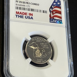 Peut inclure: Une pièce de monnaie de 25 cents du Michigan de 2004, classée PF 70 Ultra Cameo, dans un boîtier de protection. La pièce représente le contour de l'État et le texte "Great Lakes State". Le boîtier porte l'inscription "Made in the USA".