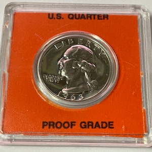 Può includere: Una moneta da un quarto di dollaro americano in argento del 1963 in una custodia di plastica trasparente con sfondo arancione. La custodia ha il testo "U.S. QUARTER" e "PROOF GRADE" stampato su di essa.