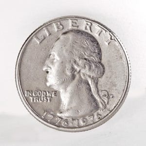 May include: A silver-colored United States quarter dollar coin featuring the profile of George Washington facing left. The text LIBERTY is at the top, IN GOD WE TRUST on the left, and the dual date 1776-1976 is at the bottom with a D mint mark.