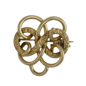 May include: A vintage gold-toned brooch with an intricate, intertwined design. The brooch features a series of looped shapes, some with delicate etched floral patterns. The pin is secured with a clasp on the back, showcasing a classic jewelry piece.