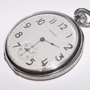 Könnte beinhalten: Eine silberne Taschenuhr mit weißem Zifferblatt und schwarzen römischen Ziffern. Die Uhr hat ein kleines Sekundenzeiger-Zifferblatt und das Wort "HOWARD" ist auf dem Zifferblatt aufgedruckt.