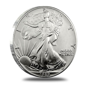 Może przedstawiać: Srebrna moneta American Eagle z wizerunkiem Lady Liberty idącej do przodu, trzymającej gałązkę oliwną w prawej ręce i pochodnię w lewej. Na monecie widnieje napis "IN GOD WE TRUST" i rok "1989".
