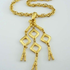 May include: A gold chain necklace with a pendant featuring a cluster of four open diamond-shaped charms with dangling tassels.