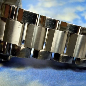 Puede incluir: Primer plano de una correa de reloj plateada con eslabones de metal pulido y cepillado.