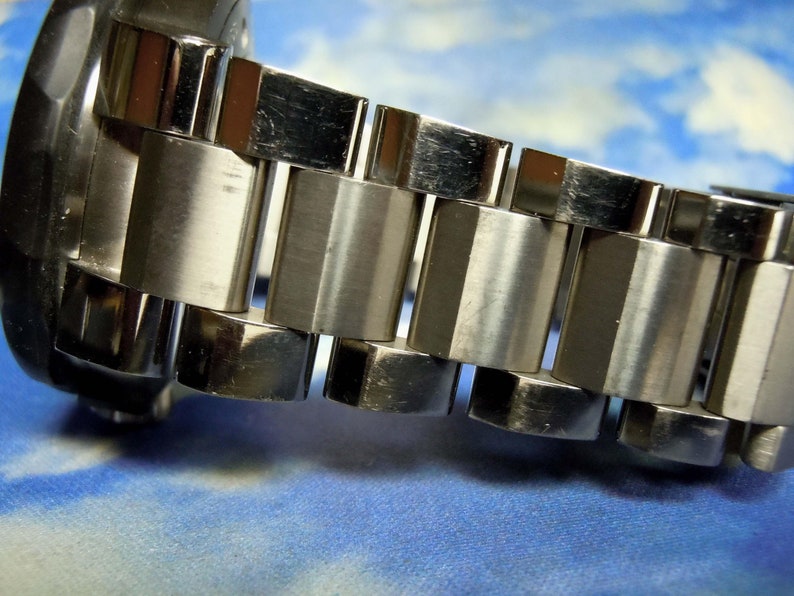 Puede incluir: Primer plano de una correa de reloj plateada con eslabones de metal pulido y cepillado.