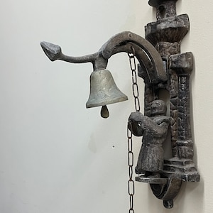 May include: A vintage metal doorbell with a bell and a chain. The doorbell is shaped like a small tower with a figure holding a bell.
