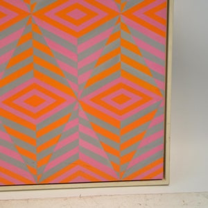 May include: Abstract geometric artwork with a repeating pattern of diamonds and chevrons. The design uses orange, pink, and grey, creating a vibrant visual effect. The artwork is framed.