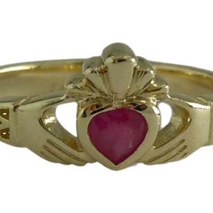 Può includere: Anello Claddagh dorato con una gemma rosa a forma di cuore. L'anello presenta due mani che stringono un cuore, sormontato da una corona. La fascia dell'anello presenta intagli decorativi. Design irlandese classico.