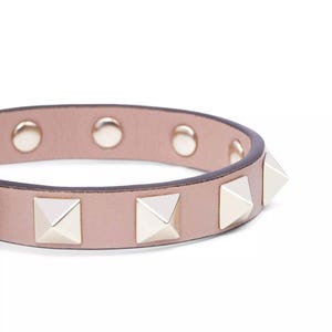 Puede incluir: Un brazalete de cuero rosa claro con tachuelas de pir&aacute;mide plateadas.